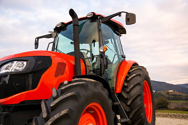 Orange tractor with weather cloudy sky.