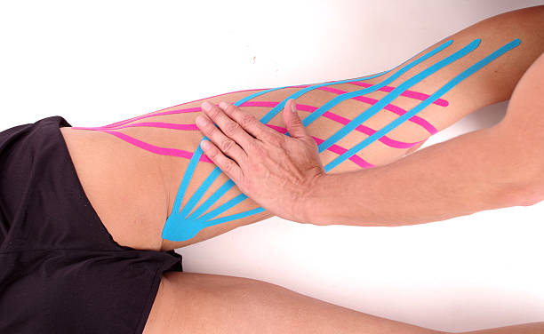 Kinesiology tape on hamstring. Physiotherapy for muscle injury Athlete laying on white background, Physiotherapist placing kinesiology tape on hamstring. Holding muscle with hands. rear viewpoint. hamstring injury stock pictures, royalty-free photos & images