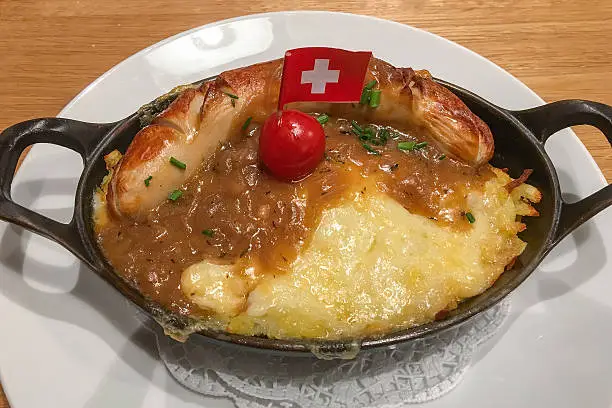 Traditional Swiss dinner of a veal sausage with potato rosti covered in melted cheese