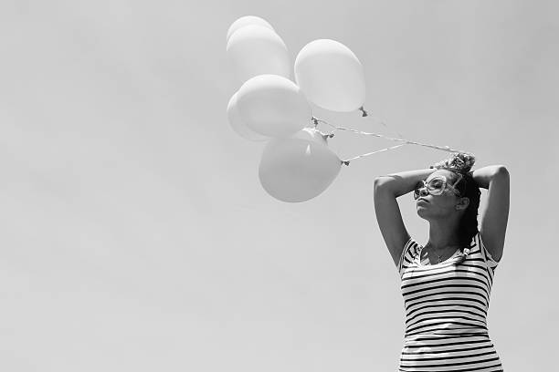 Happy little girl 2-3 year old wearing trendy, stylish dress and holding balloon standing over white background. Looking at camera. Happiness. Birthday celebration