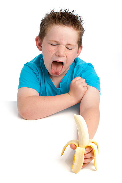 Yound boy not happy about eating a banana.