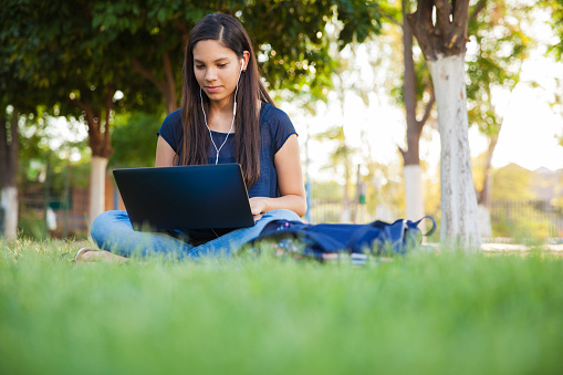 Beautiful teenage girl using a laptop and earbuds outdoors