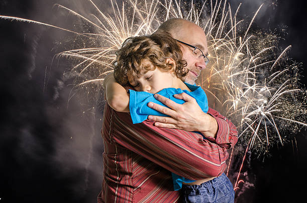 Son and father hug with firewoks in background