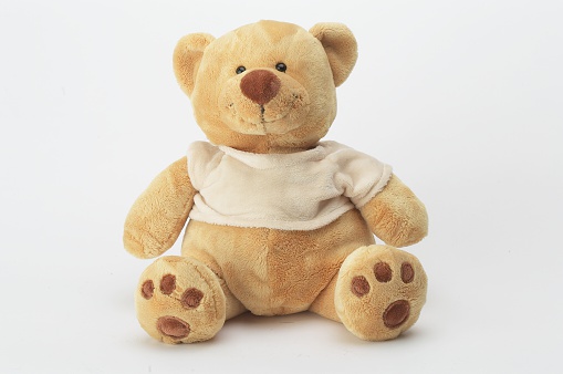 A smiling teddy bear wearing a white t shirt and displaying the paw pads on his feet. He appears to be a soft velvety texture.
