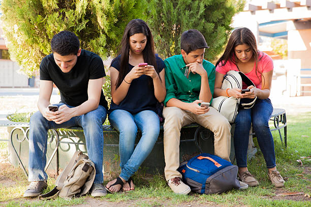 Teens busy with cell phones Group of teenage boys and girls ignoring each other while using their cell phones at school teenagers only stock pictures, royalty-free photos & images