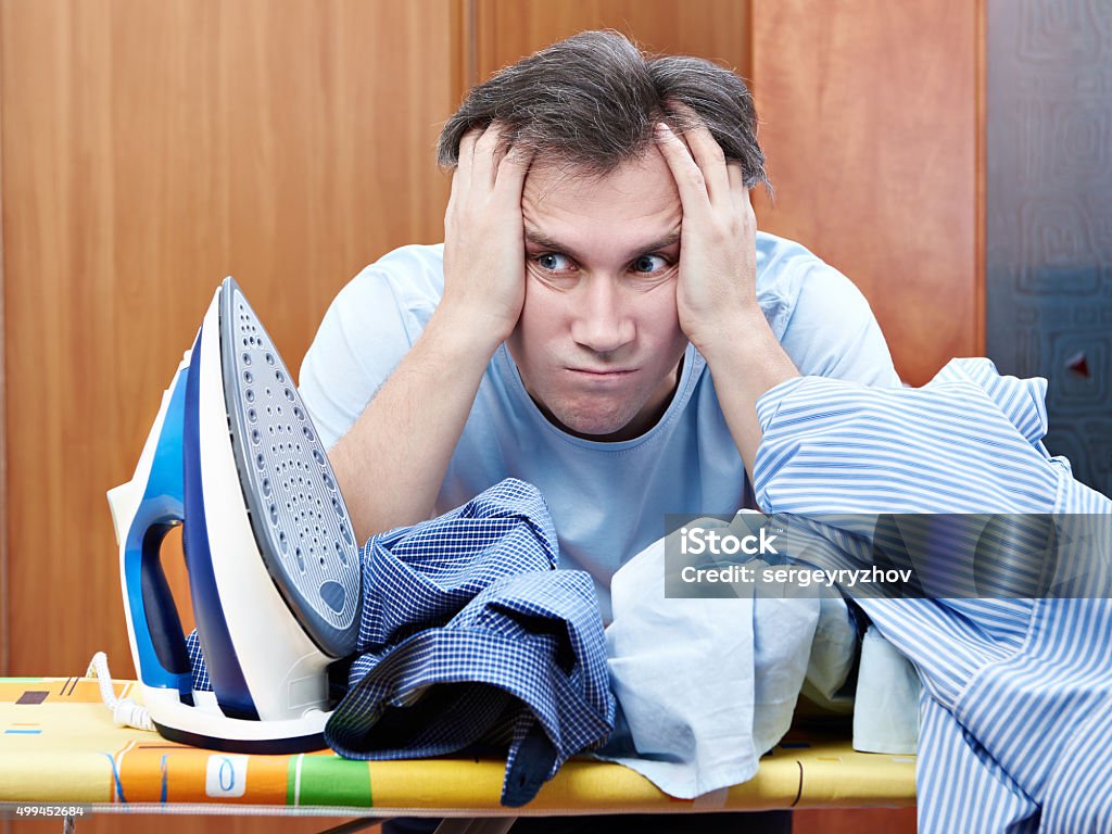 Sad man with pile of crumpled shirts and iron Sad man with pile of crumpled shirts and iron. Housework 2015 Stock Photo