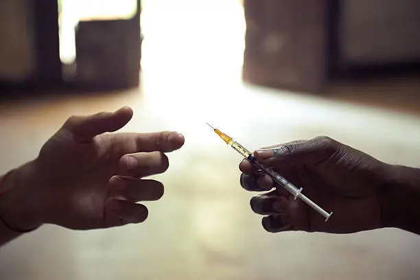 People abusing drugs, with African american man and caucasian guy sharing the same syringe to inject heroin