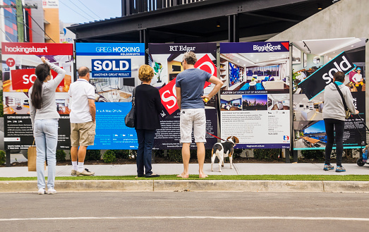 Melbourne, Australia - November 28, 2015: Visitors reading a row of estate agent signs outside a newly-renovated apartment building at 5 Commercial Rd, South Yarra. Formerly a derelict hotel, the site was the focus of Series 11 of popular Channel Nine TV series The Block. a reality renovation contest.