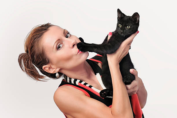 Attractive young woman holds a black kitten on hands. Studio shooting on a white background.