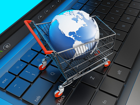 Shopping cart with a globe standing on laptop computer keyboard. Online shopping concept.