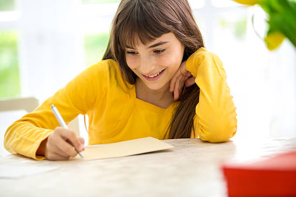 Cute smiling girl writing a letter sitting at desk