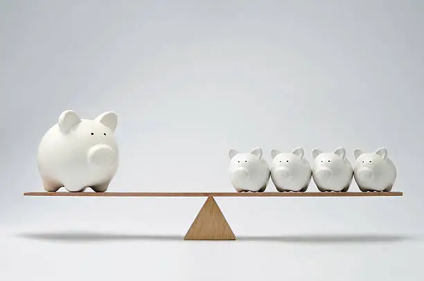 Small piggy banks and large piggy bank balancing on a seesaw