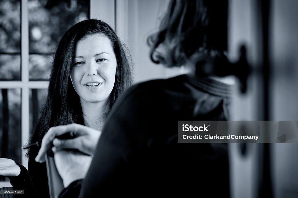 Young Woman Talking To a Colleague. Black and white portrait of two women talking to each other in a workplace environment. It could be used to illustrate an interview or a counselling situation. Horizontal format with a point of view of looking over the shoulder of one of the subjects, photographed in a candid and relaxed style. 30-34 Years Stock Photo