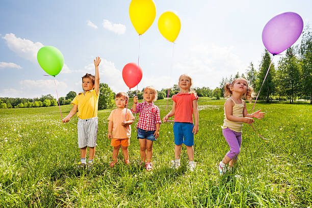 istock Five cute children with balloons in green field 499467951