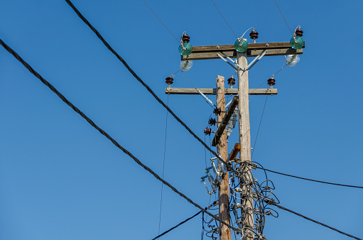 Old wooden telegraph post support a tangle of overhead power lines.