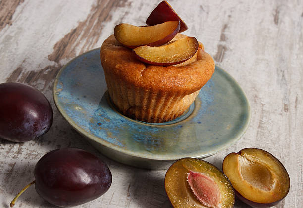 Fresh muffins with plums on plate on old wooden background stock photo