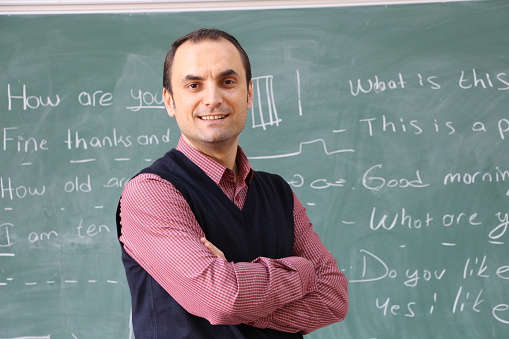 The teacher in the classroom on greenboard background. Male teachers show the board with his hand. teacher smiling. 