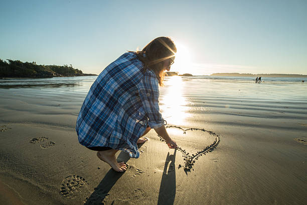 istock Young woman on beach drawing heart shape on sand-sunset 499484642