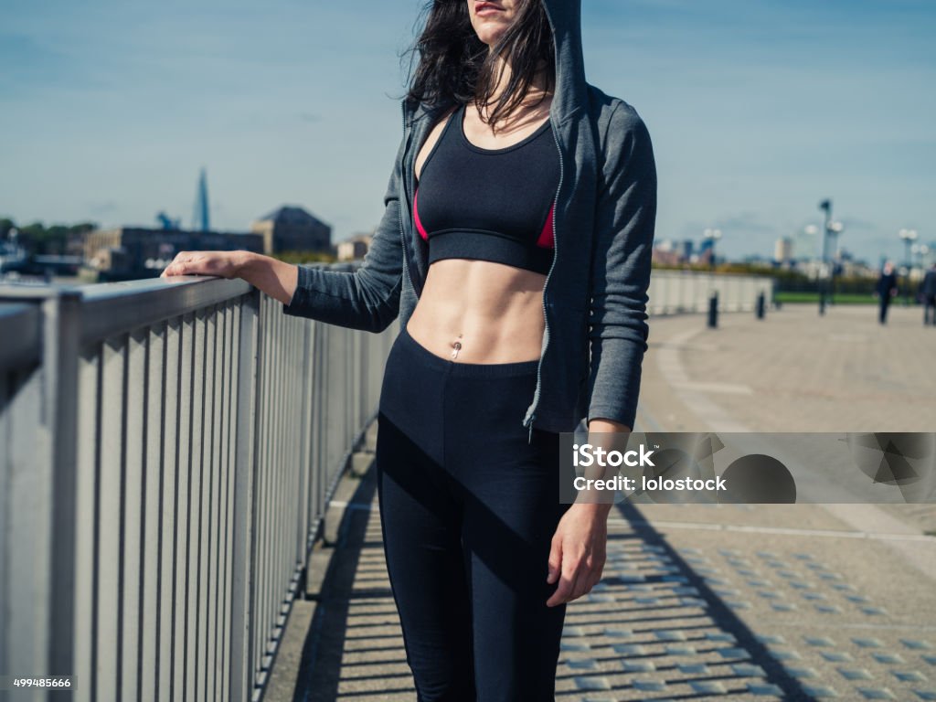 Fit and athletic young woman in city A fit and athletic young woman with toned abs is standing in the city by a fence 2015 Stock Photo