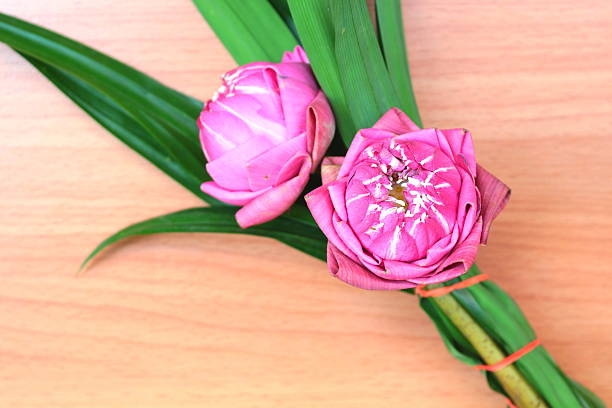 Bunch of pink lotus flowers bind with green pandan leaves on wooden background.