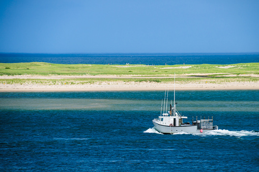 A commercial fishing boat travels past a fragile barrier beach in Aunt Lydia's Cove as it heads back to its mooring in Chatham, Massachusetts.