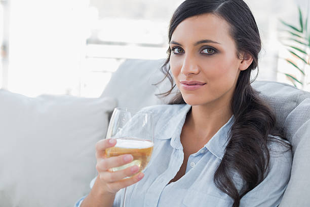 istock Pretty brunette drinking white wine sitting on sofa 499492857