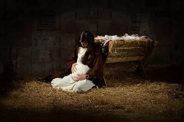Pregnant Mary leaning on the manger on Christmas Eve