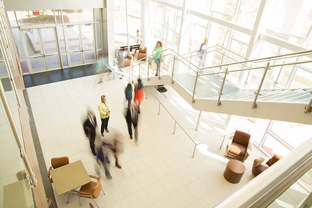 Busy people in business office, bank or shopping mall. Busy people 'on the go' in office area, bank, or shopping mall. Mixed ages, ethnicities, and dress.  African descent woman center.  Other unrecognizable people walking. bank entrance stock pictures, royalty-free photos & images