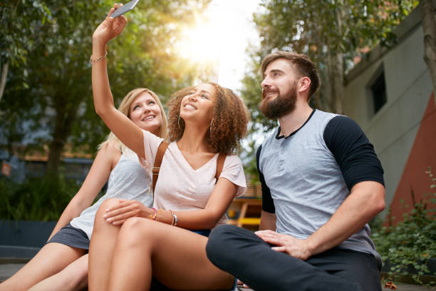 Three young friends taking a selfie with cellphone. Multiracial group of young people having fun together while sitting outdoors.