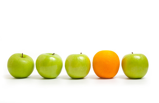 green apples lined up with one orange on a white background