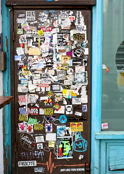 A door to a closed down shop in London covered in stickers and graffiti