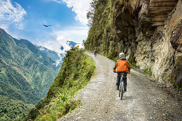 Adventure travel downhill biking road of death Bike adventure travel photo. Bike tourists  ride on the "road of death"  downhill track  in Bolivia. In the background sky circles a condor over the scene. hell photos stock pictures, royalty-free photos & images