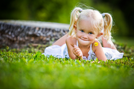 Funny baby girl in a wreath of yellow dandelions on the background of spring grass.