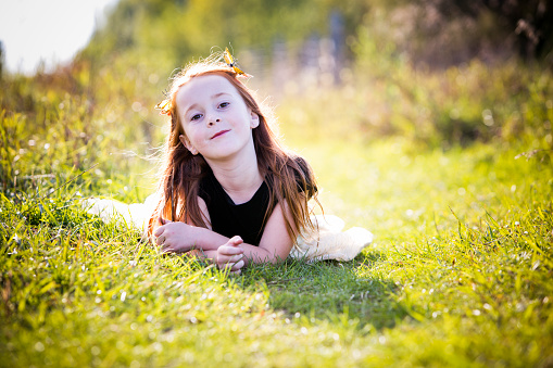 Cheerful little girl laying on grass and enjoying a beautiful spring day at the public park.
