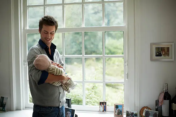 Happy young father looking at newborn baby in cottage