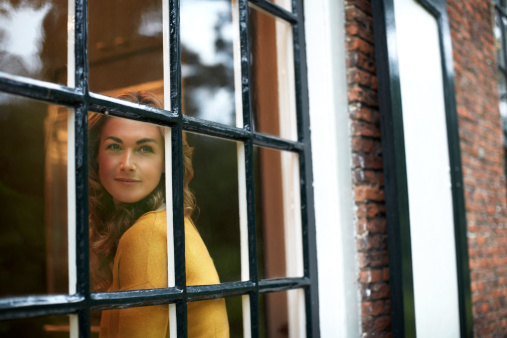 View of thoughtful young woman looking trough cottage window