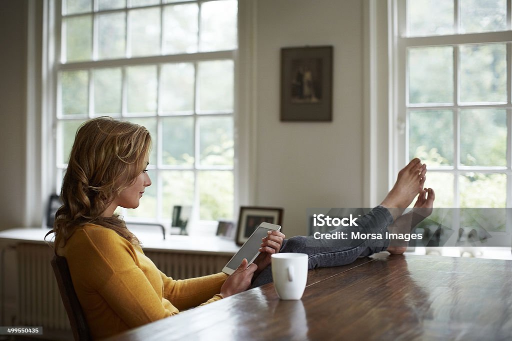 Woman using tablet while relaxing in cottage Full length of young woman using digital tablet while relaxing at table in cottage Digital Tablet Stock Photo