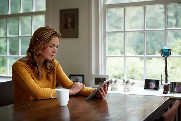 Young woman using digital tablet while having coffee at table in cottage