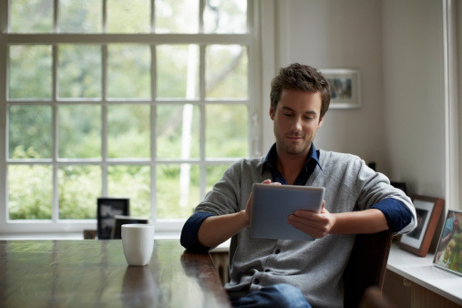 Young man using digital tablet while having coffee at table in cottage