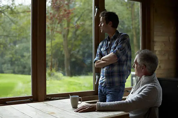 Senior man with son looking through window in cottage