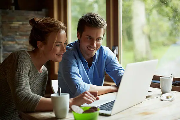 Happy young couple using laptop while having coffee at table in cottage