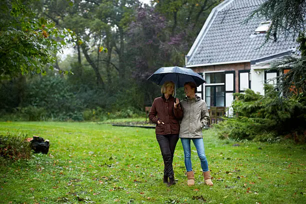 Full length of happy mother and daughter with umbrella standing outside cottage