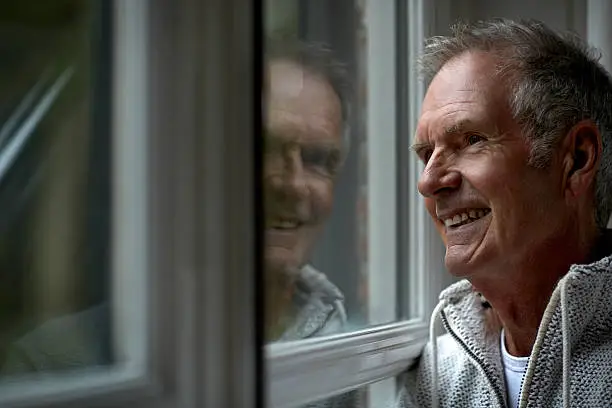 Happy senior man looking through window in cottage