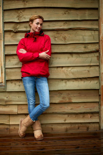 Full length portrait of confident woman standing arms crossed against wooden wall