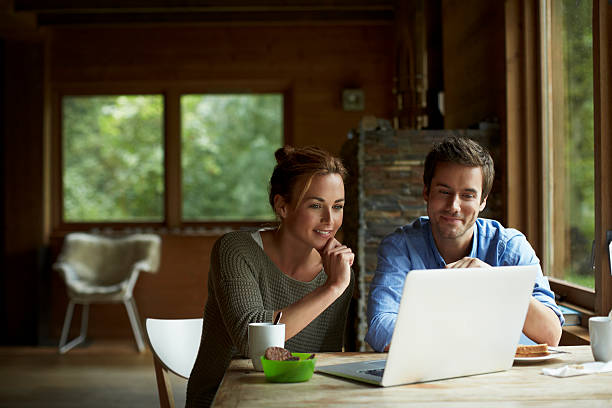 couple using laptop at table in cottage - computer couple laptop home interior foto e immagini stock