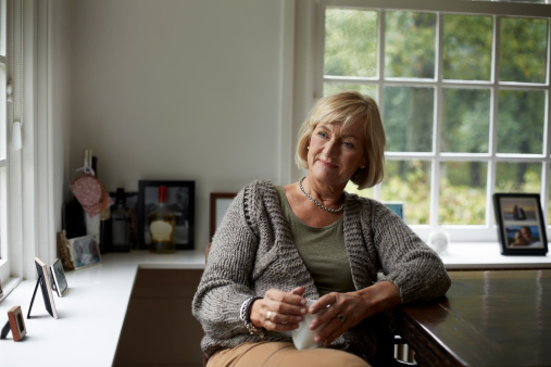 Thoughtful senior woman with coffee cup relaxing at table in cottage
