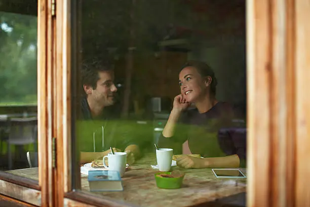 View of young couple having breakfast at table in cottage through window