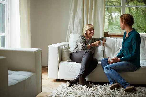 Happy mother and daughter having coffee on sofa in country house