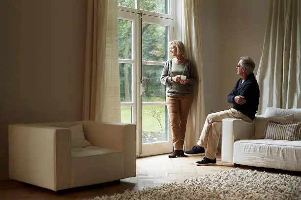 Relaxed senior couple looking out through door in house