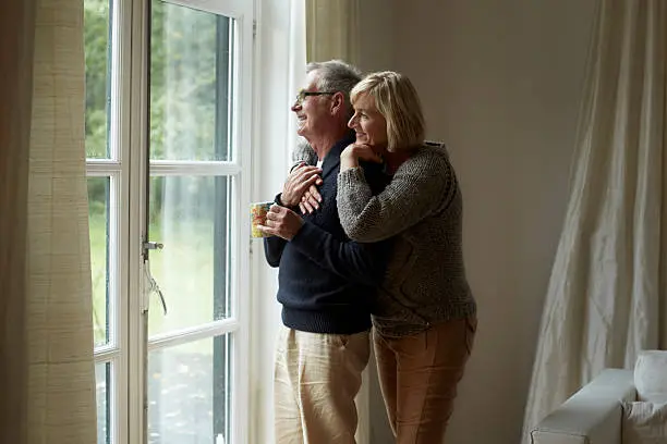 Happy senior couple looking out through door at home